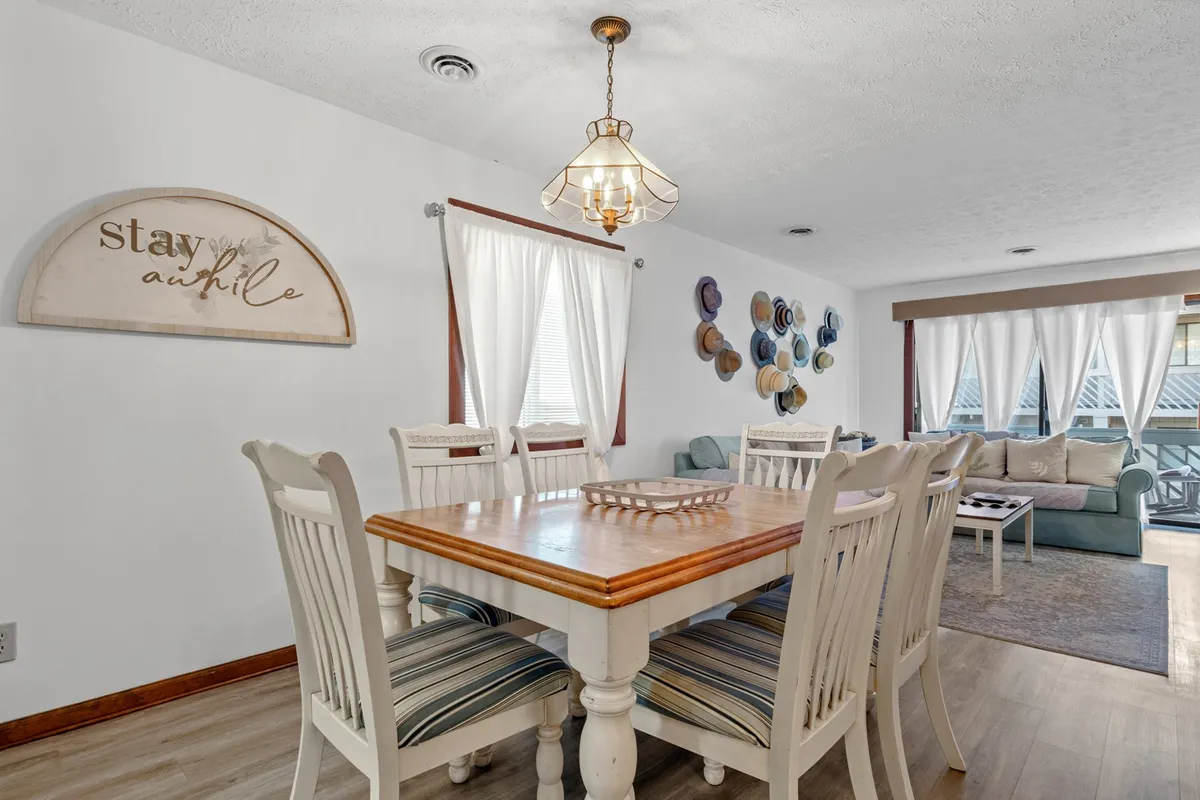 A view of the dining area set beside a decorative wall and adjacent to a cozy sofa seating area. The warm lighting and stylish light fixture create an inviting spot for group meals, board games, or casual conversations.
