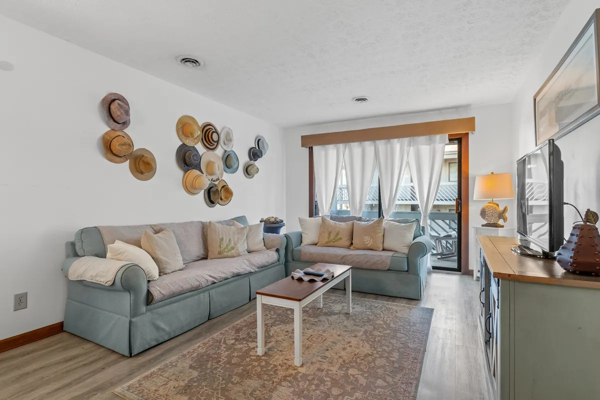 A cozy living area featuring a sofa with plush cushions, a decorative wall with hats, a wooden coffee table, and a flat-screen TV. Warm lighting and thoughtful décor create an inviting ambiance for relaxation or socializing.