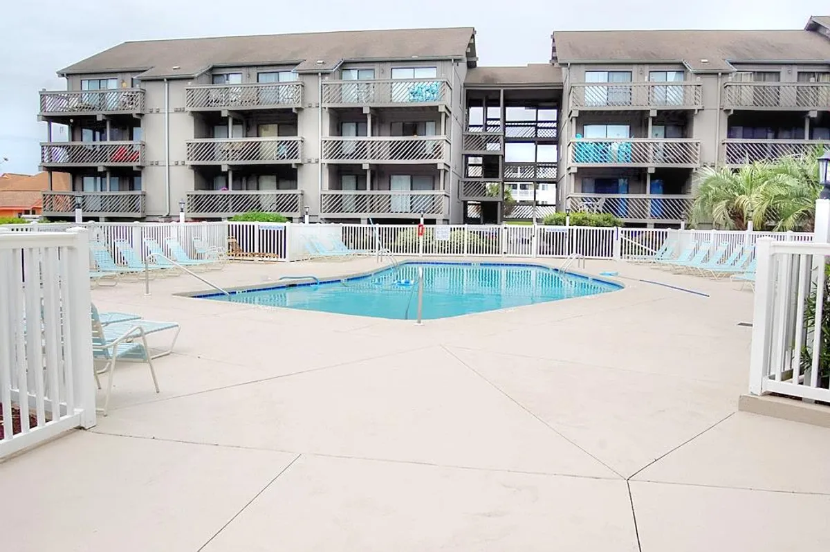 The swimming pool is surrounded by palm trees, balconies, and loungers, suggesting a social yet relaxed community setting. The stilted building design and pool area evoke a resort-like environment ideal for both personal relaxation and connecting with neighbors.