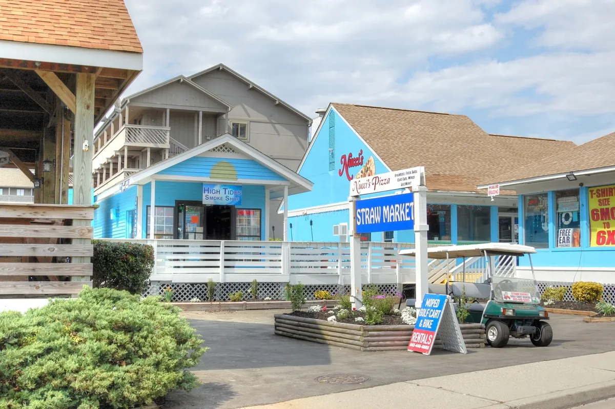 This exterior shot features a stretch of colorful storefronts, a golf cart, and signage, evoking the casual and lively vibe of local shopping and dining areas. The image hints at unique shopping experiences, alfresco dining, and discovering the vibrant community spirit.